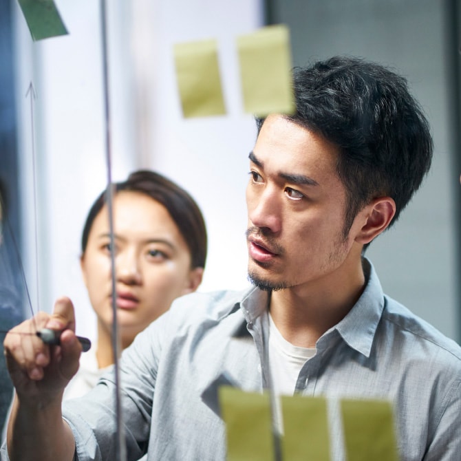 ガラスボードにアイデアを書き込みながら打ち合わせをする男女